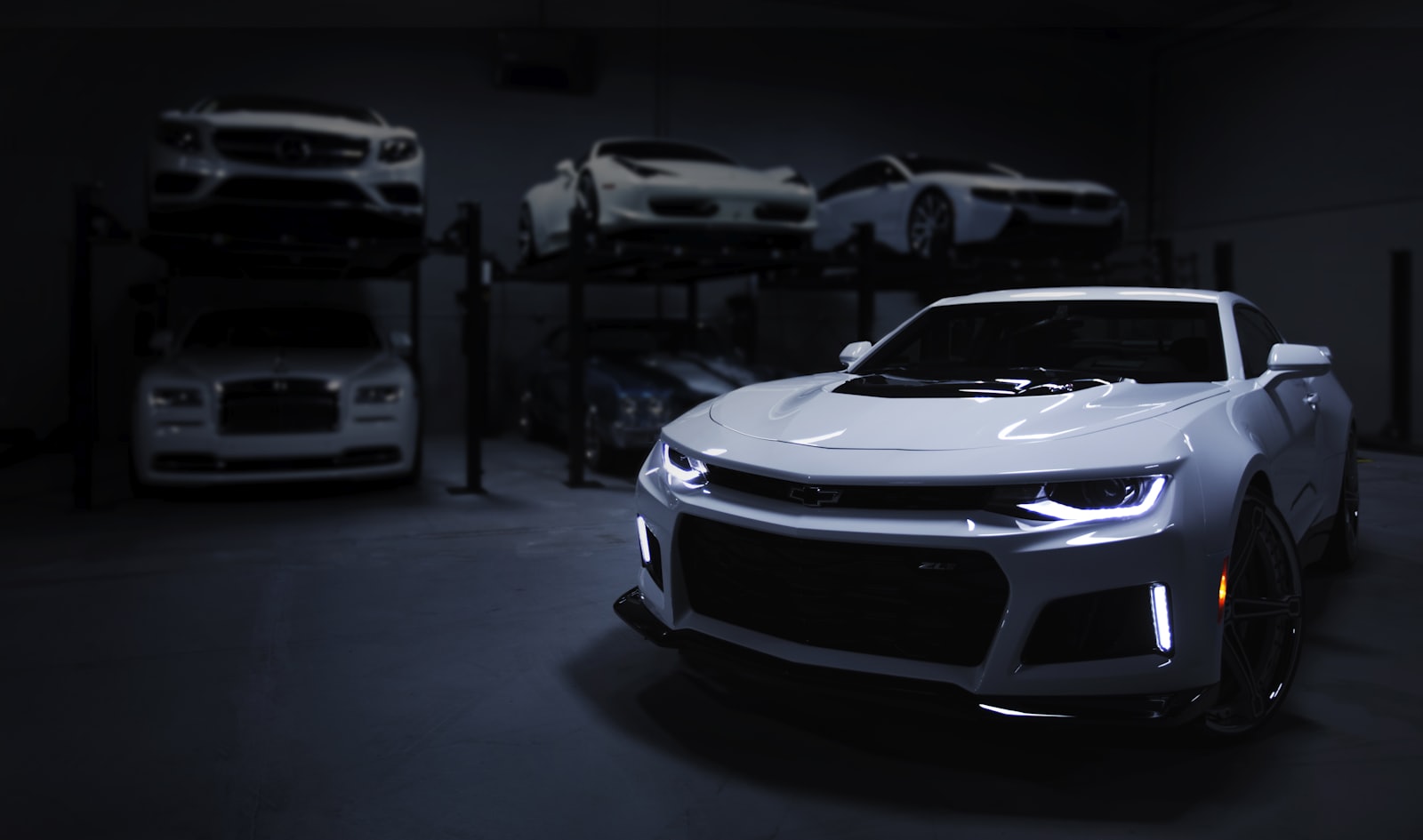 White sports car in a dark garage with cars stored on lifts