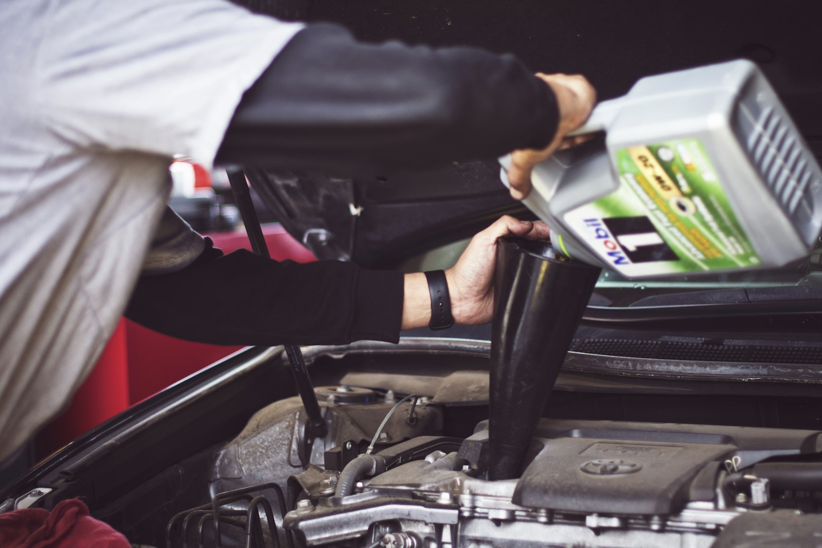 Technician topping up engine oil under the bonnet of a car