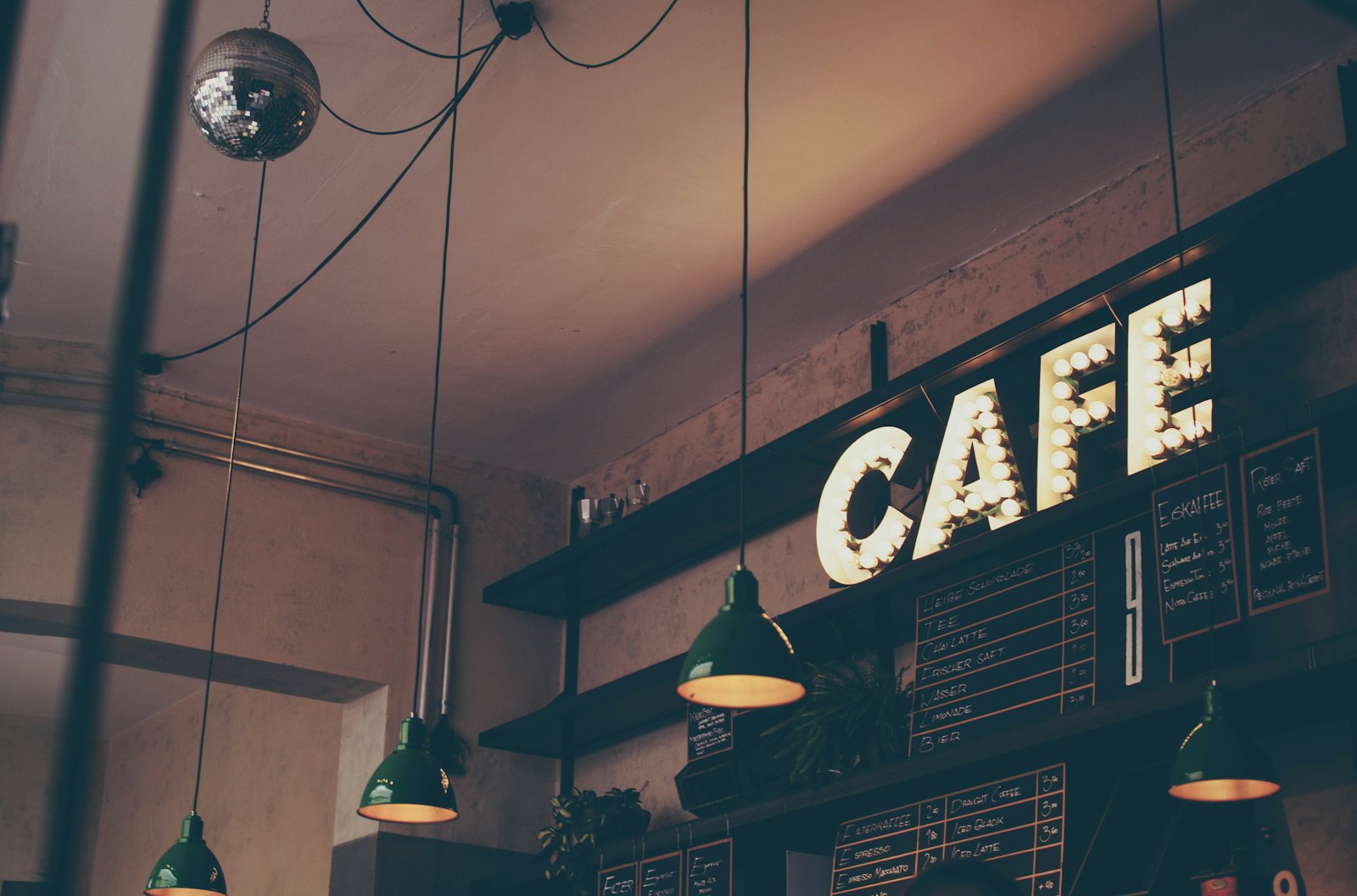 Warmly lit cafe interior with a glowing CAFE marquee sign and hanging green lamps