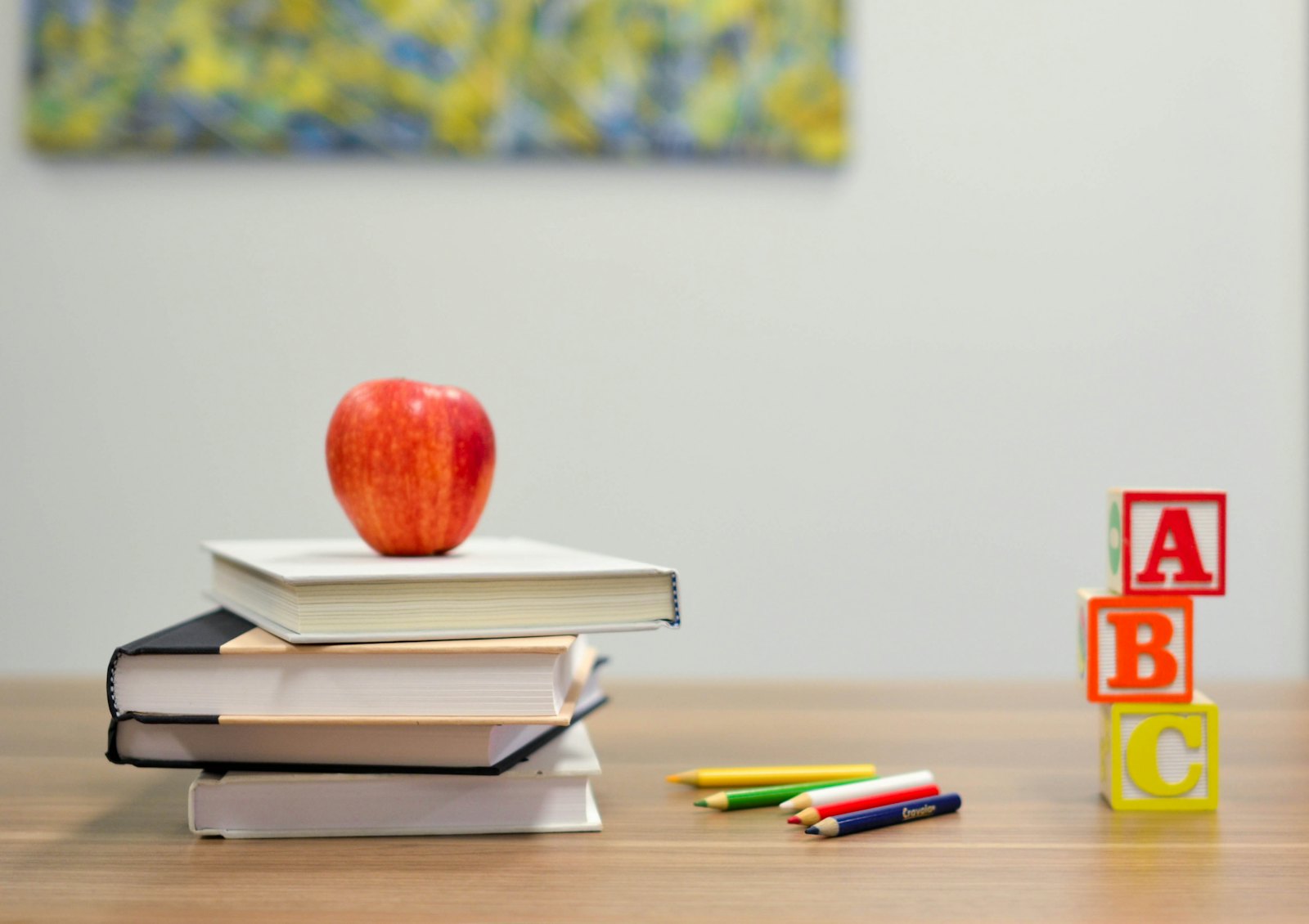 Stack of school books with an apple, colour pencils and ABC blocks on a desk