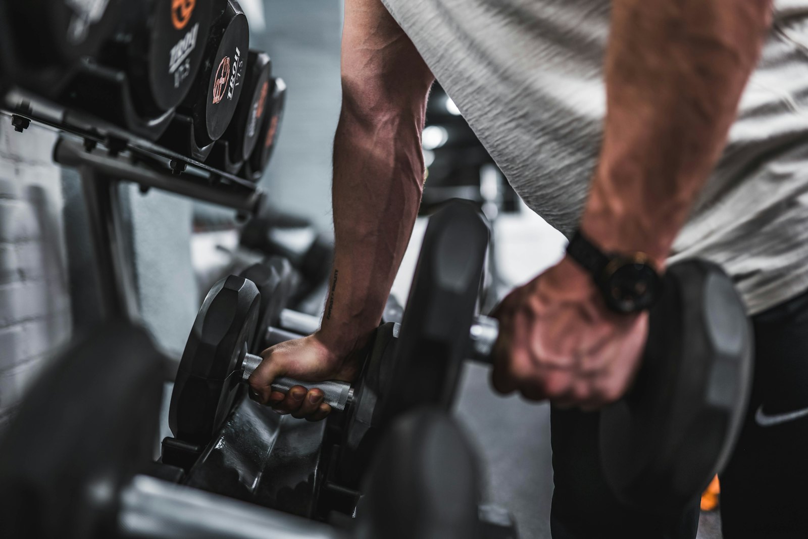 Coach lifting a pair of heavy dumbbells from a rack