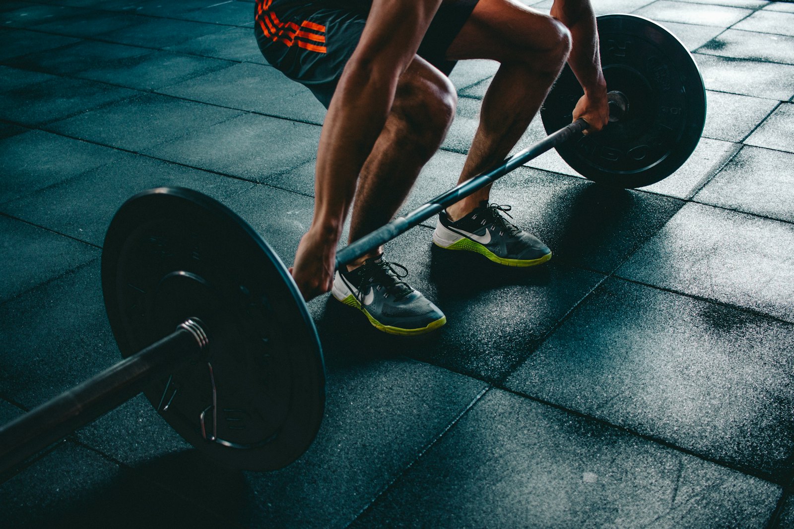 Coach gripping a loaded barbell in deadlift setup position on a dark gym floor