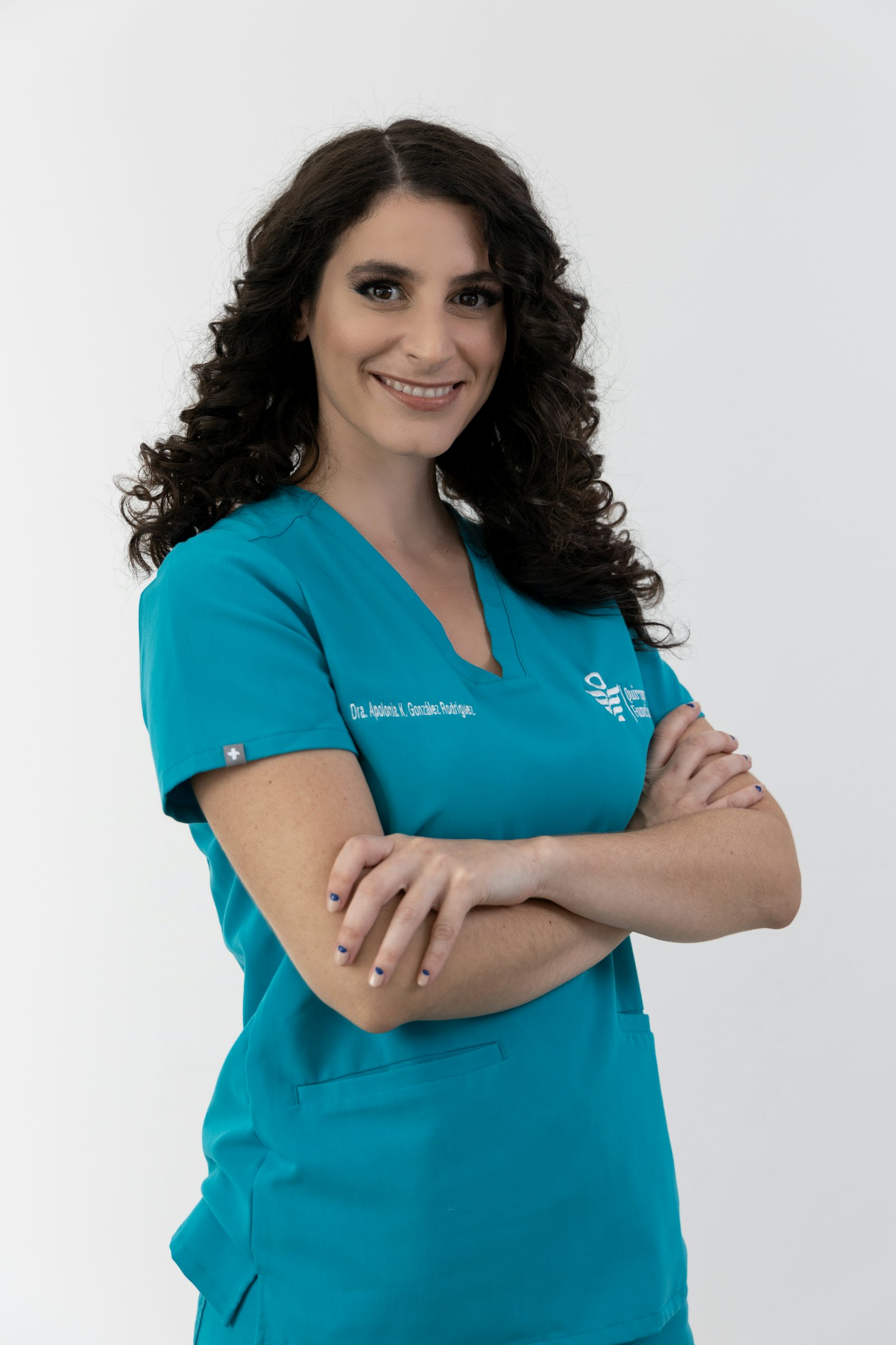 Portrait of a smiling female doctor in teal scrubs with arms crossed