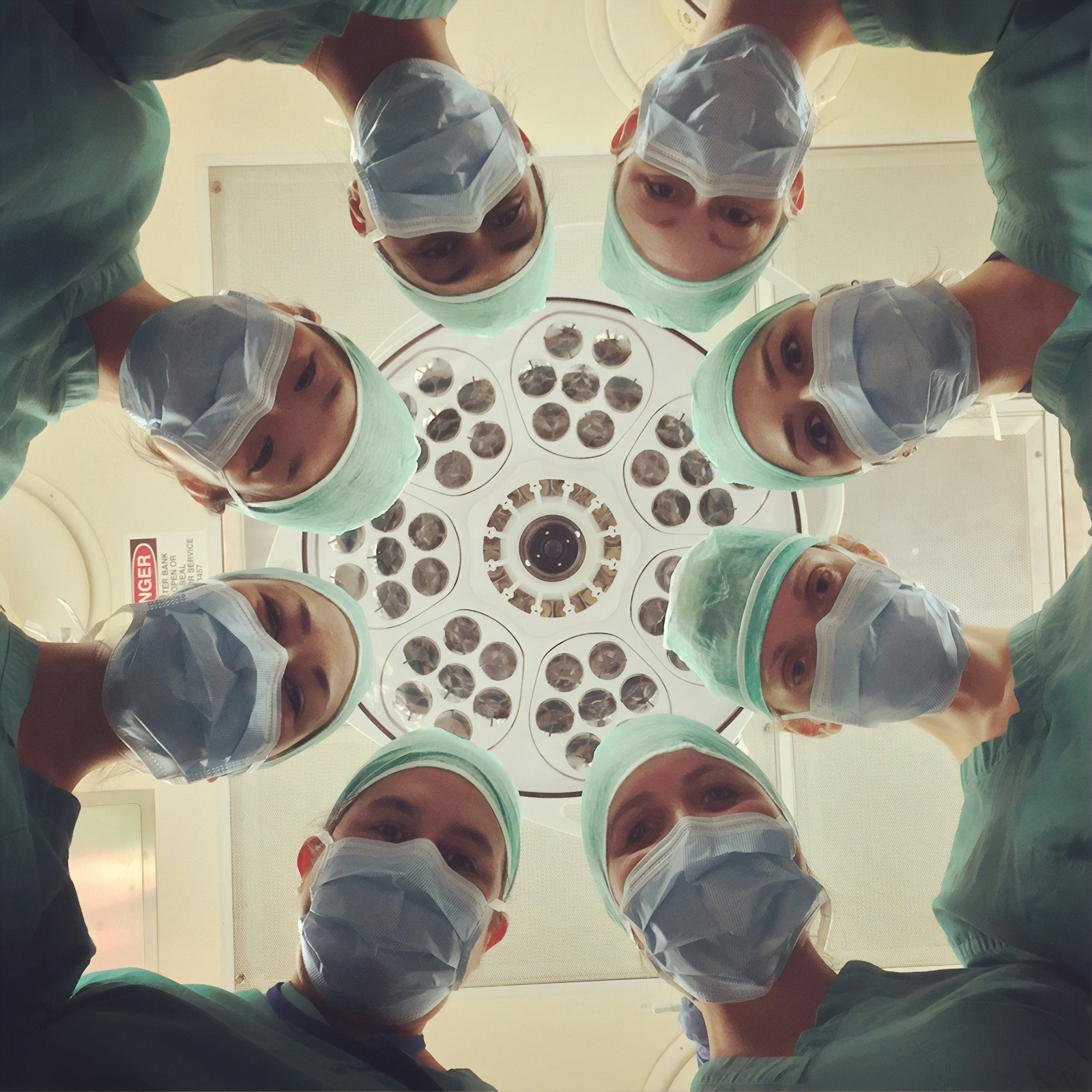 Surgical team in scrubs and masks gathered in a circle beneath an operating theatre light
