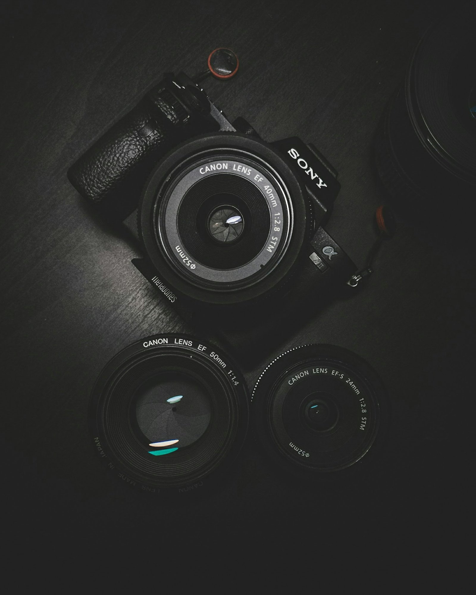 Camera body and prime lenses arranged on a black table, lit low and moody