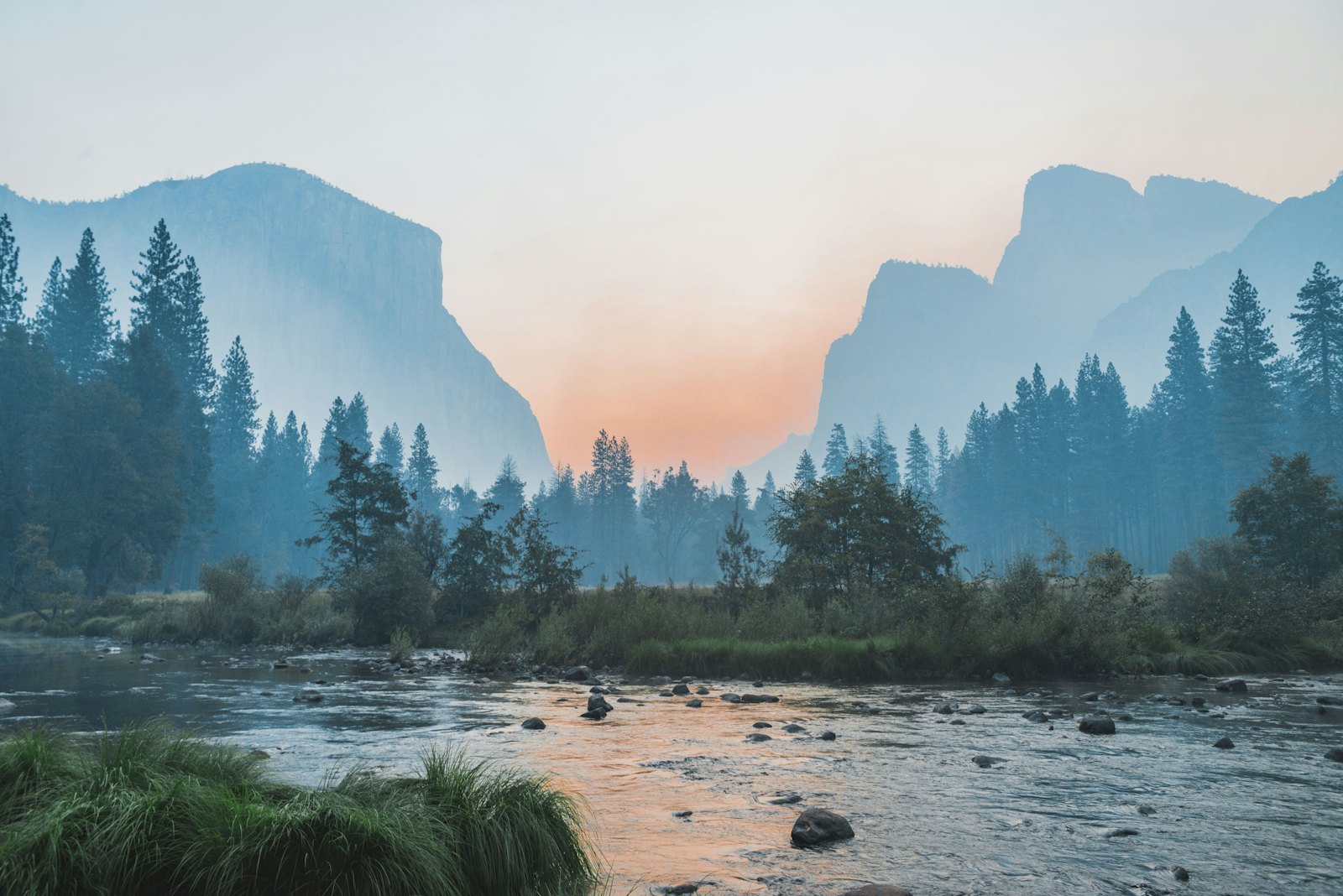 Misty valley at dawn with granite cliffs, pine forest, and a river in soft light