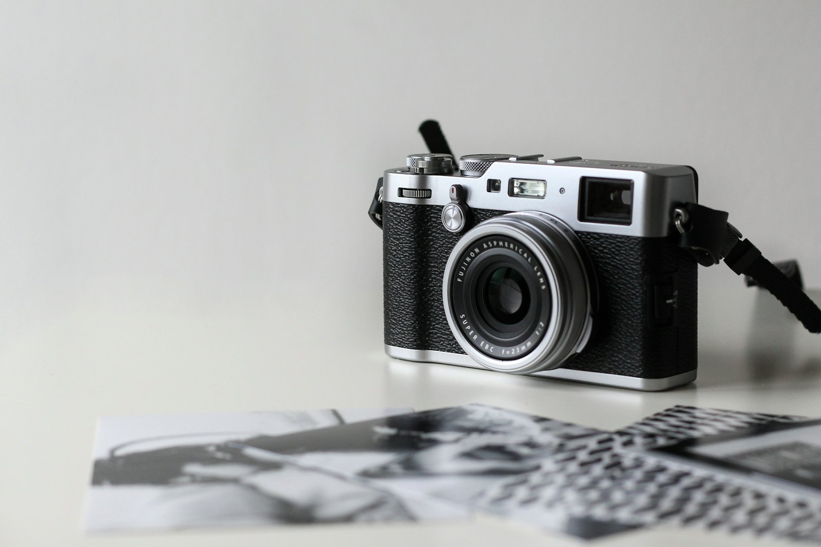 Silver and black rangefinder camera on a white table beside black-and-white prints