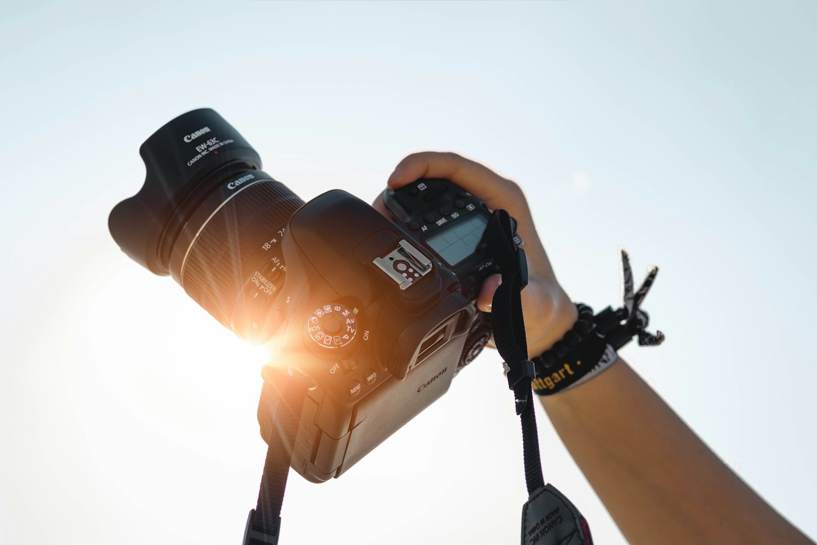 Photographer's hands lifting a camera against a bright sky with sun flare through the lens
