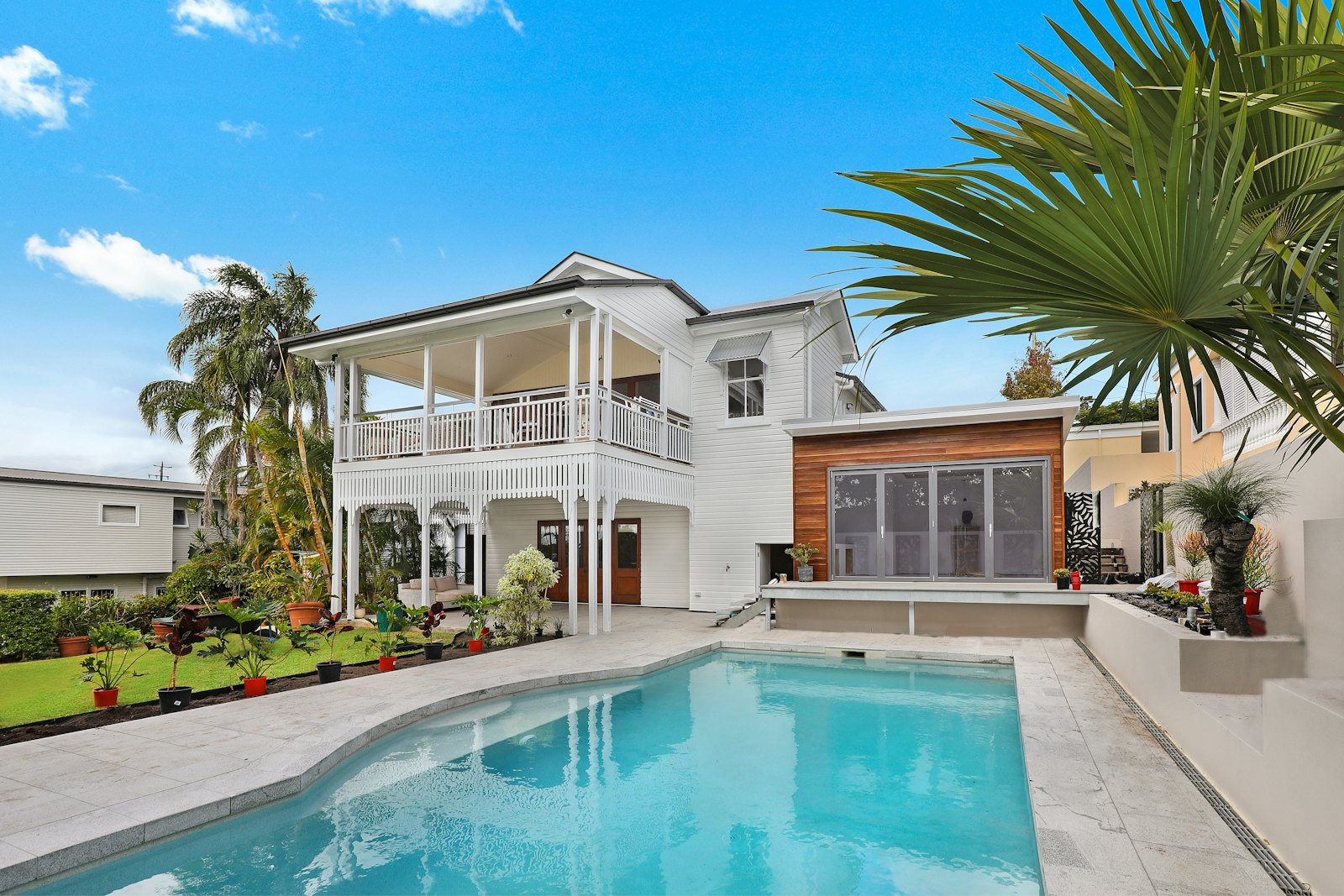 Tropical white two-storey home with wide balconies, palm trees, and a private pool