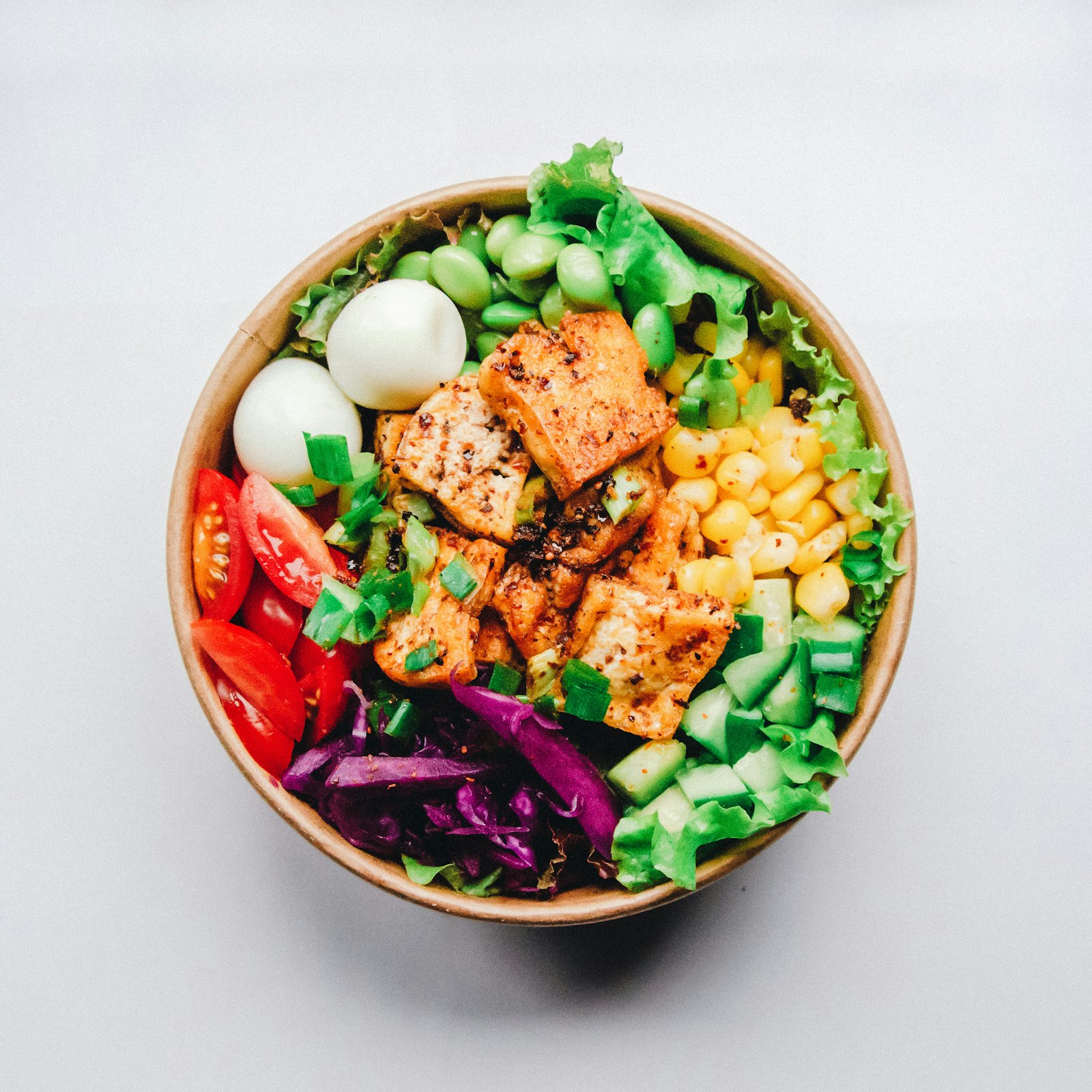 Colourful bowl of crispy tofu, edamame, corn, tomatoes and greens