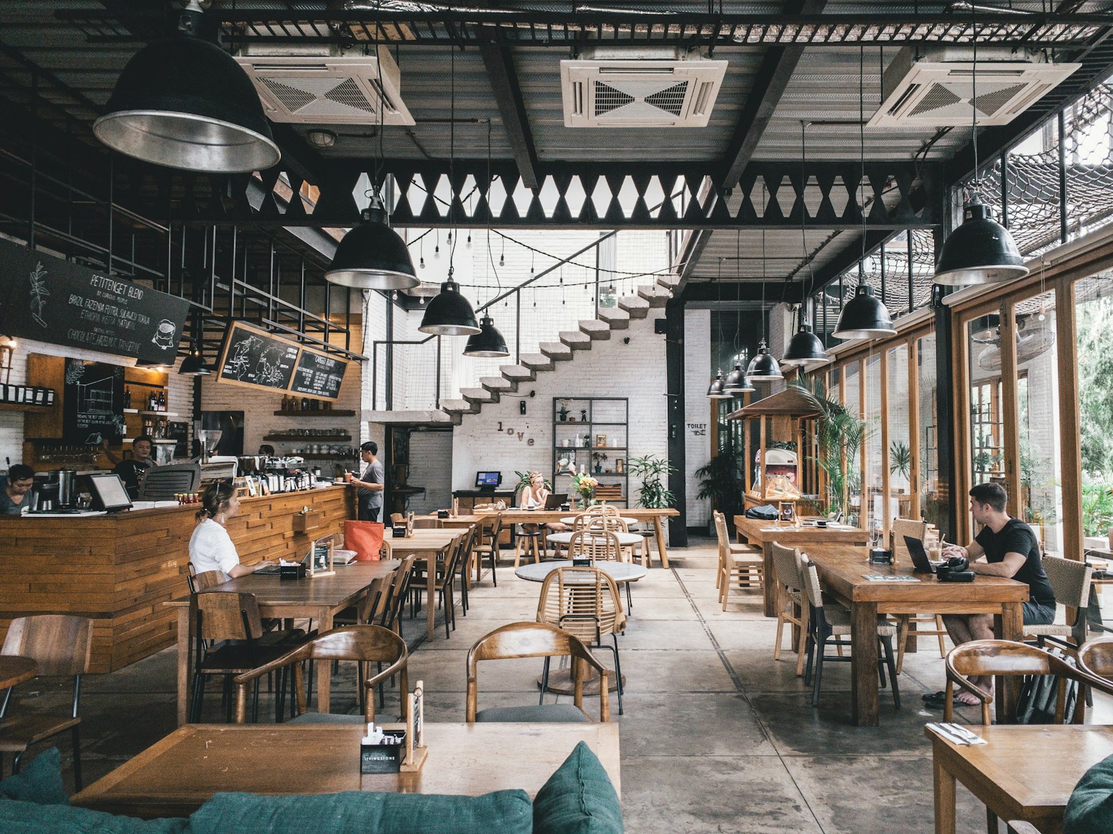 Airy dining room with long wooden tables, pendant lamps and an open bar