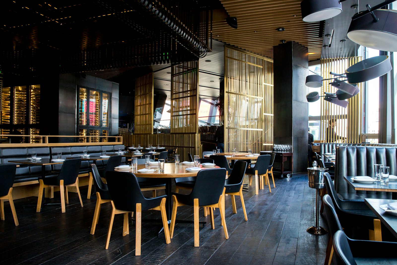 Moody restaurant dining room with dark timber ceilings, brass screens and leather banquettes