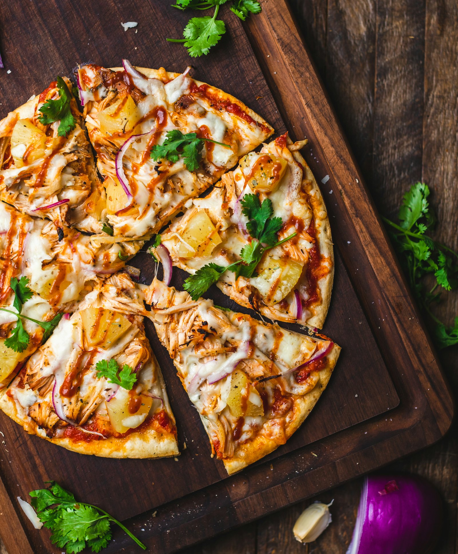 Rustic flatbread pizza with pulled chicken and herbs on a dark wooden board