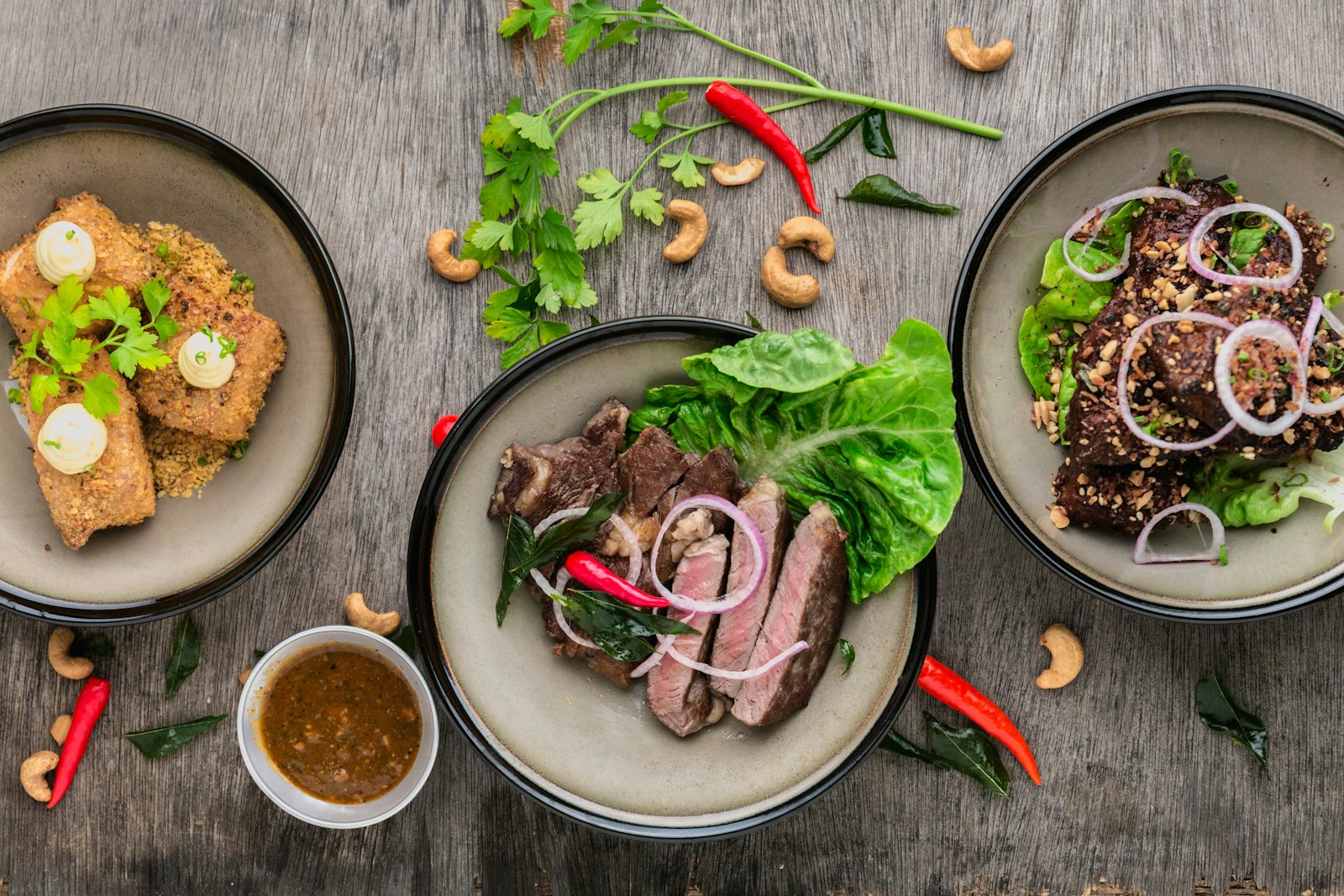 Three plated dishes of grilled meat and crispy bites with chillies and herbs