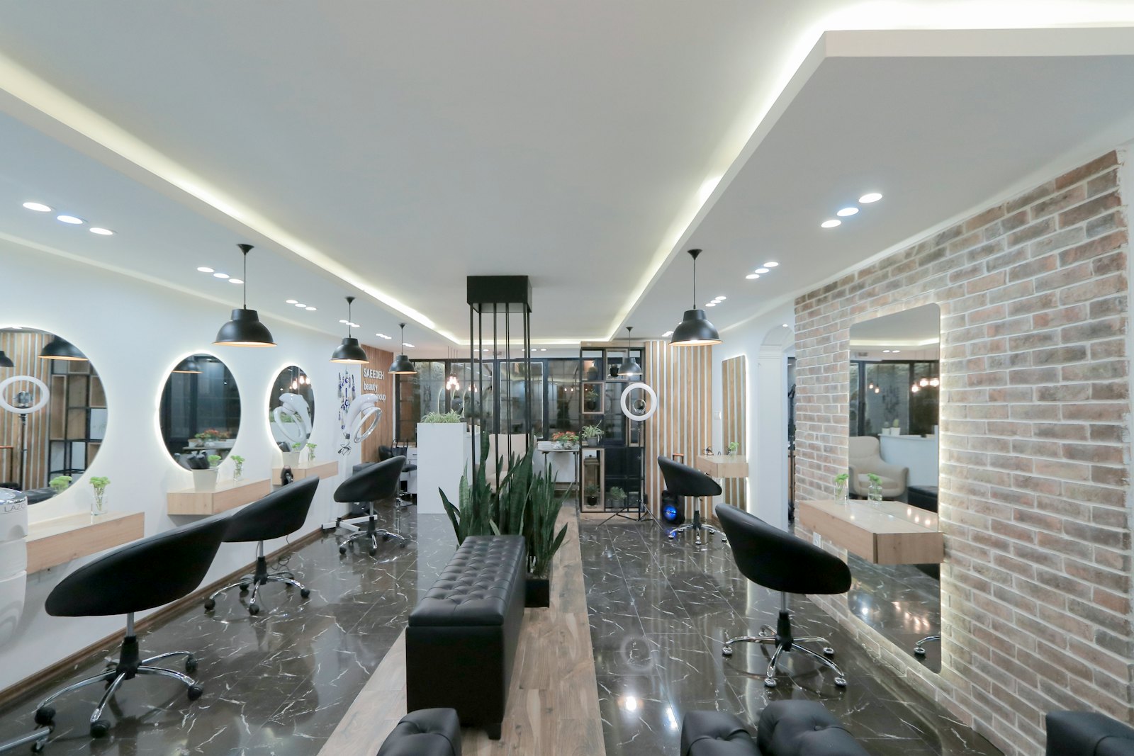 Bright, modern salon floor with round backlit mirrors, black styling chairs, and greenery