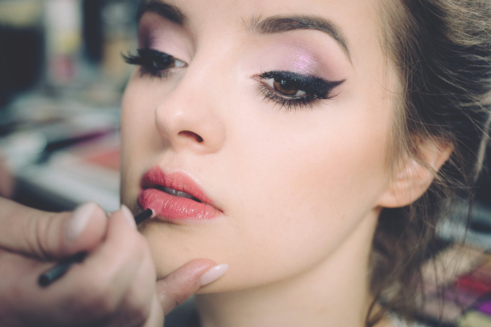 Makeup artist applying rose lipstick to a client with soft pink eyeshadow