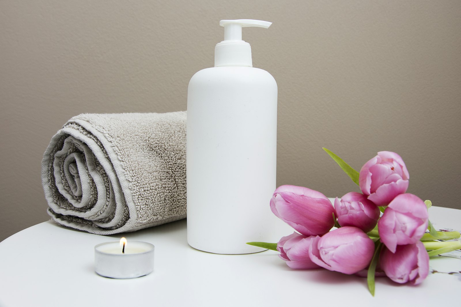 Spa still life of a rolled towel, lotion bottle, lit tealight candle, and pink tulips