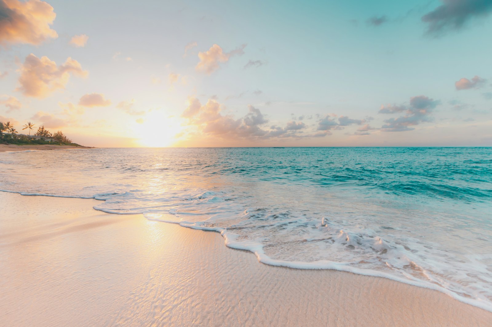 Gentle waves washing onto a sandy beach at sunset with turquoise sea