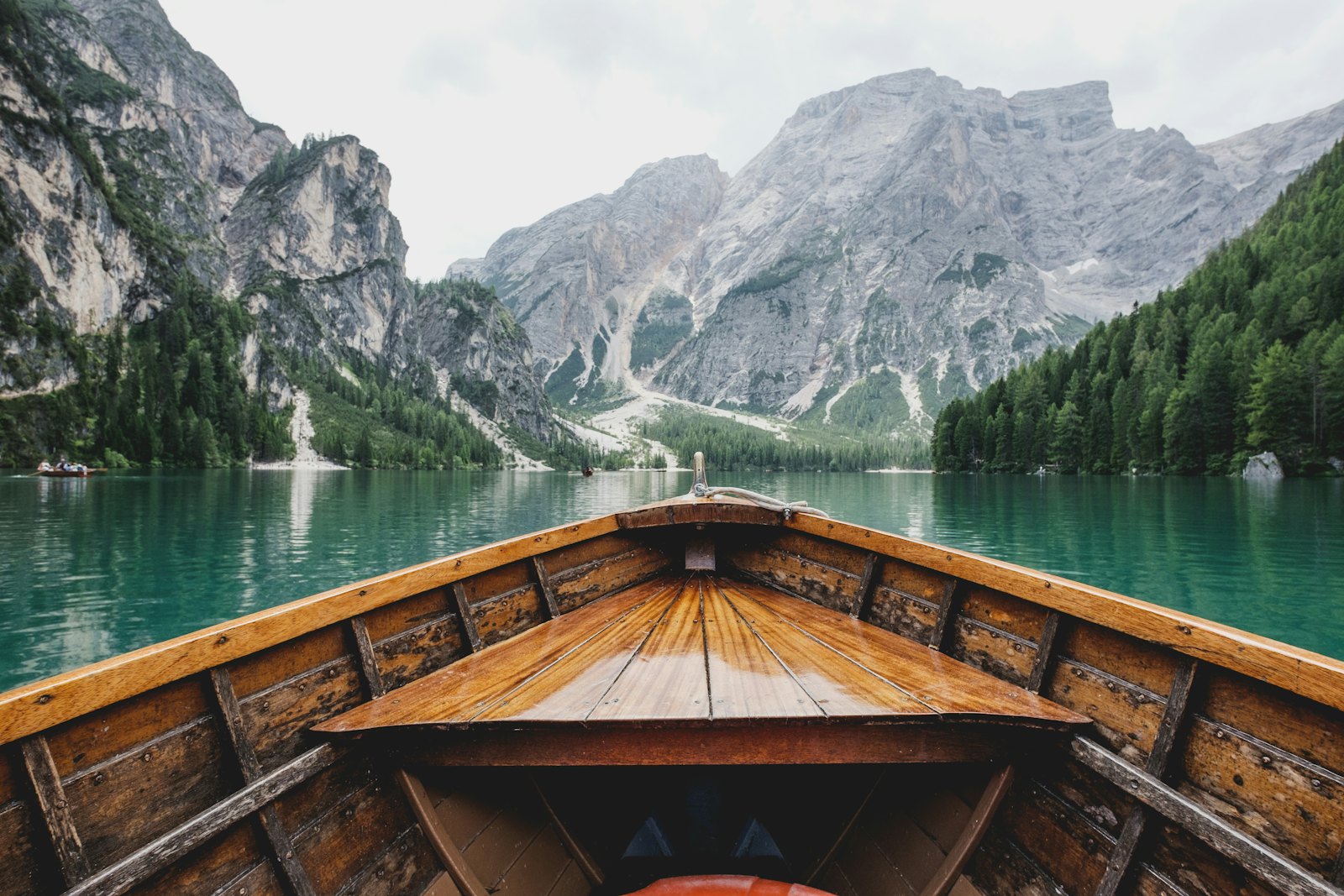 Wooden rowing boat gliding across a turquoise alpine lake beneath rocky peaks