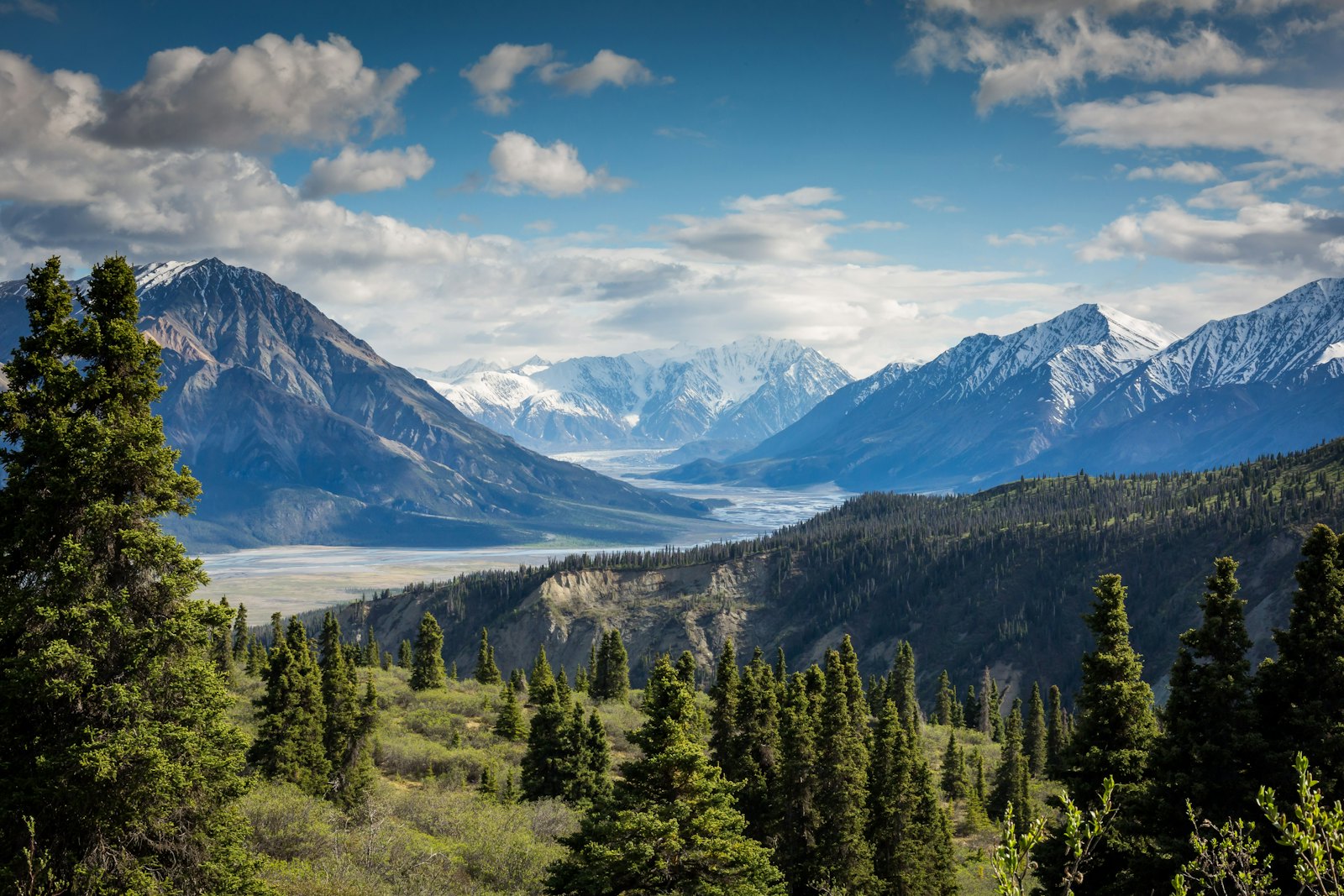 Snow-capped mountain range above a forested valley and winding river