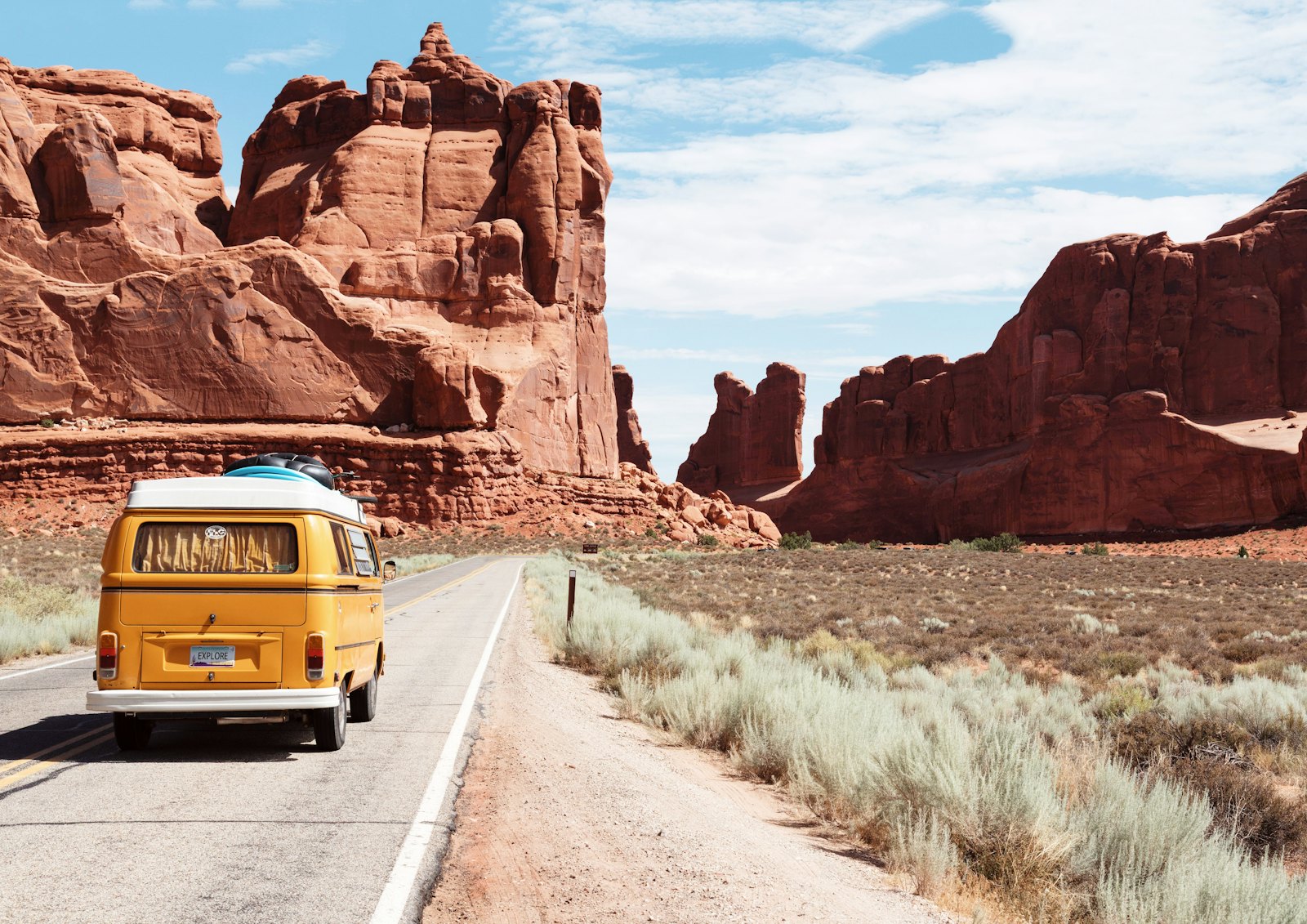 Yellow campervan driving a desert highway between red rock canyons
